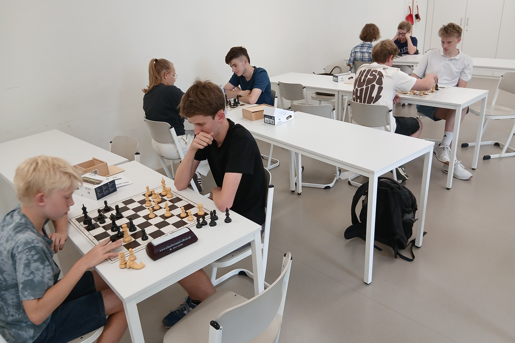An mehreren weißen Tischen spielen Schüler gegeneinander Schach