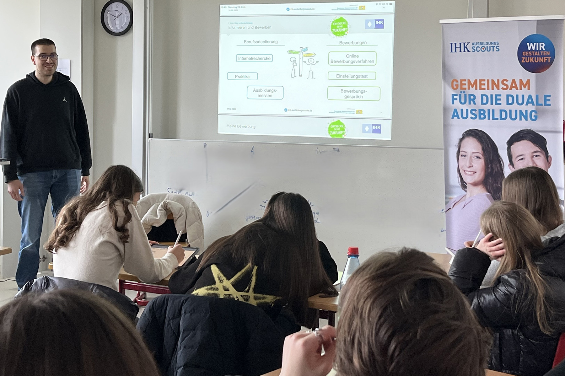 Mann steht an der Tafel vor einer Schulklasse