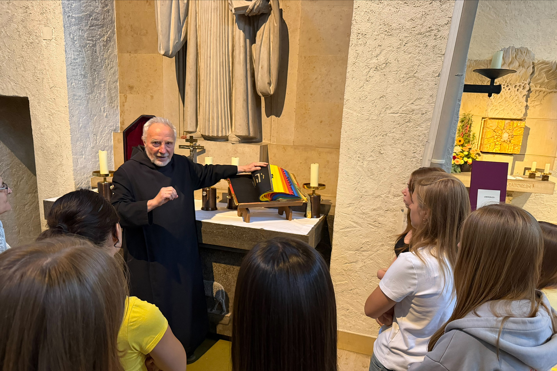 Mönch an einem Altar in der Kirche, er blättert durch ein Buch mit bunten Seiten