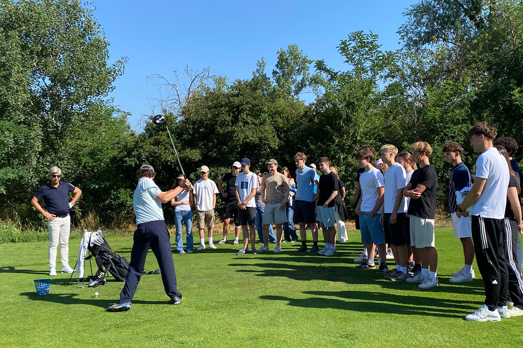 Eine Gruppe von Schülern beobachtet einem Mann beim Abschlag auf dem Golfplatz