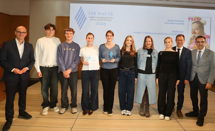 Schülerinnen und Schüler stehen mit drei Männern vor einer Leinwand