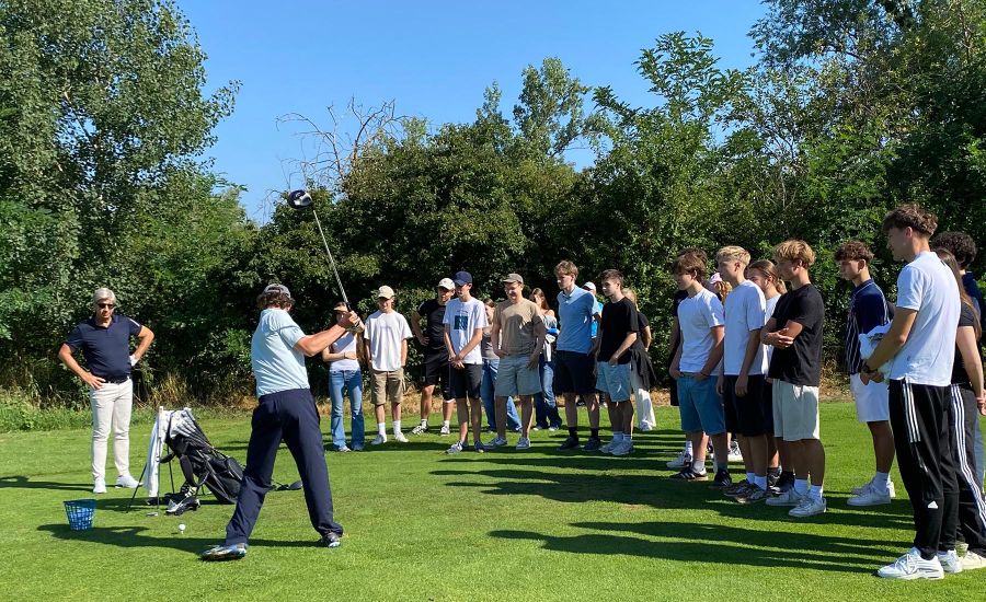Eine Gruppe von Schülern beobachtet einem Mann beim Abschlag auf dem Golfplatz