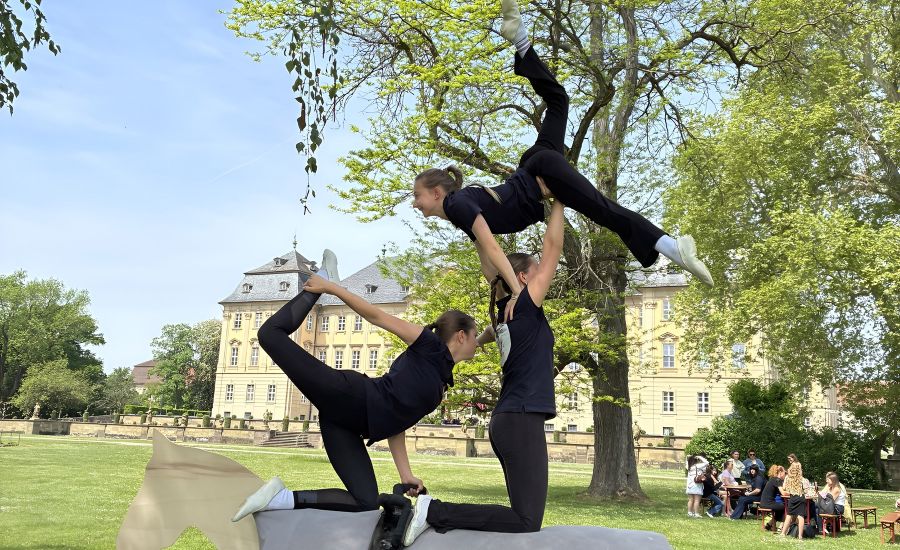 Drei junge Frauen sind auf einem Holzpferd in einer akrobatischen Pose zu sehen